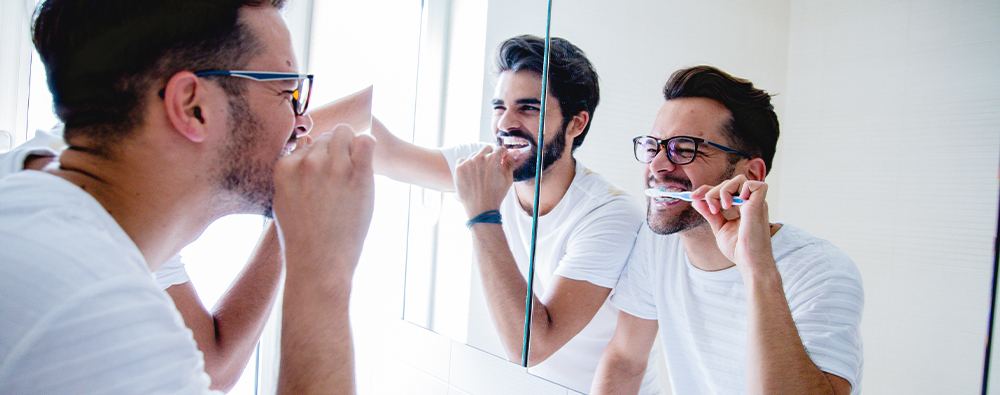 An LGBTQ+ couple brushes their teeth while looking in the mirror.